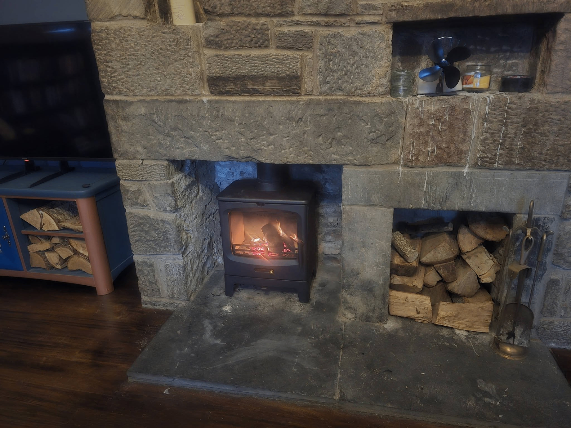 Compact stove fitted in rustic stone fireplace